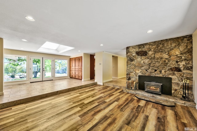 unfurnished living room with a skylight, a fireplace, wood-type flooring, and french doors