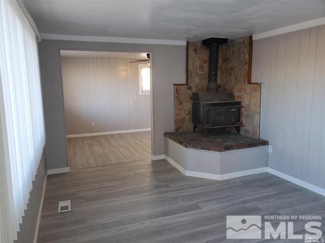 unfurnished living room featuring crown molding, visible vents, a wood stove, wood finished floors, and baseboards