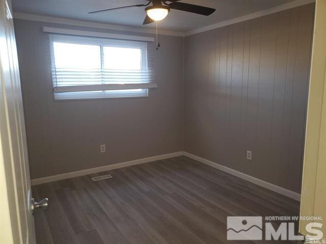 empty room featuring ornamental molding, dark wood-type flooring, and baseboards