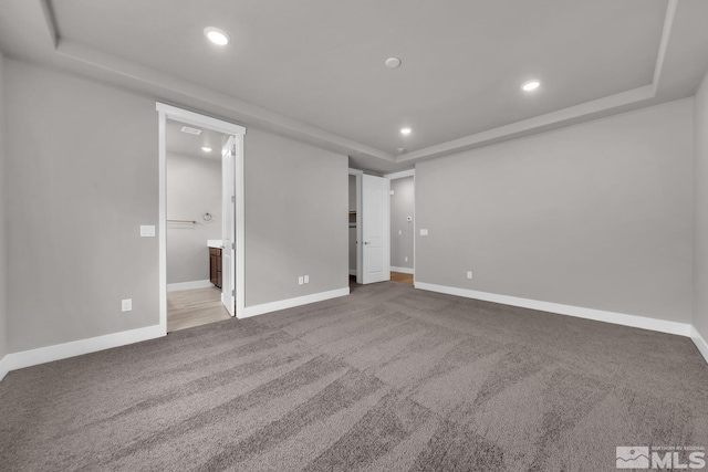 unfurnished bedroom featuring light carpet, ensuite bath, and a tray ceiling