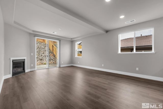 unfurnished living room featuring a healthy amount of sunlight, dark wood-type flooring, and beam ceiling