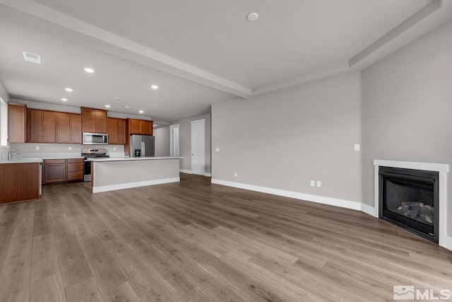 unfurnished living room featuring sink, beam ceiling, and light hardwood / wood-style floors