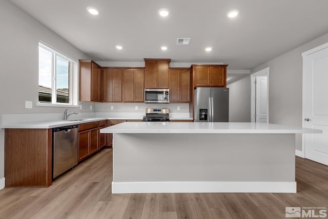 kitchen with a kitchen island, appliances with stainless steel finishes, sink, and light hardwood / wood-style floors