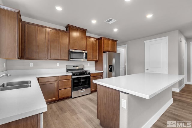 kitchen featuring stainless steel appliances, a center island, sink, and light wood-type flooring