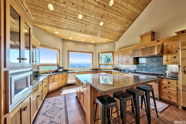 kitchen with a kitchen island, decorative backsplash, stainless steel appliances, wall chimney range hood, and wooden ceiling