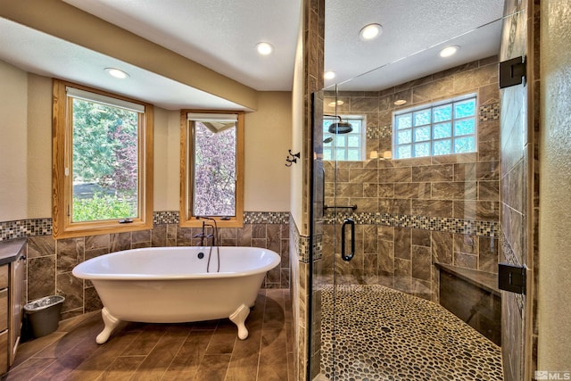 bathroom with tile walls, vanity, shower with separate bathtub, and a textured ceiling