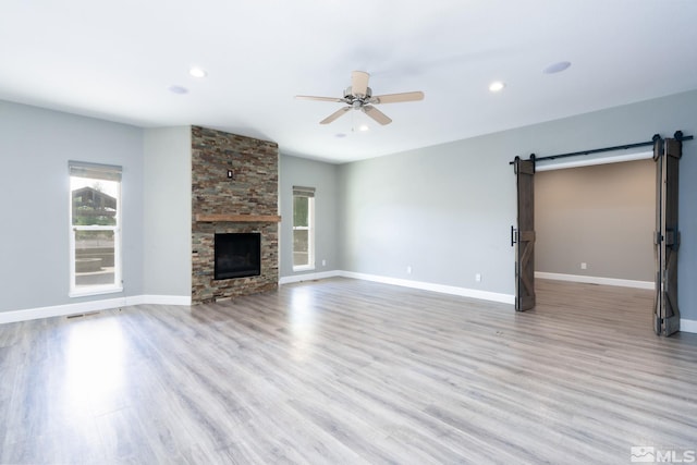 unfurnished living room featuring a fireplace, light hardwood / wood-style flooring, a barn door, and ceiling fan