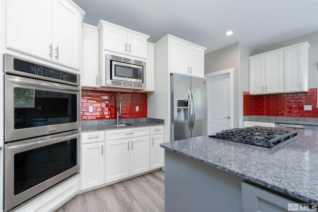 kitchen with stainless steel appliances, white cabinetry, sink, and light hardwood / wood-style floors