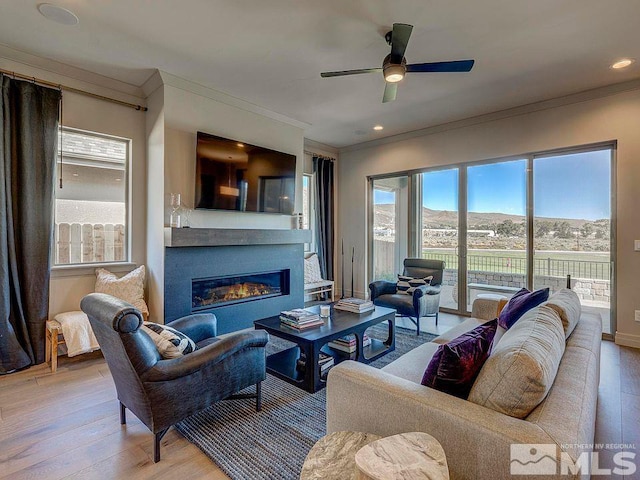 living room with light hardwood / wood-style floors, ornamental molding, and ceiling fan