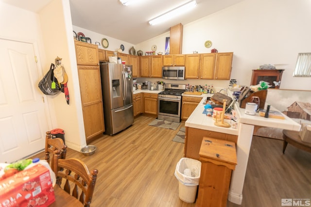 kitchen with vaulted ceiling, appliances with stainless steel finishes, light wood-type flooring, and kitchen peninsula