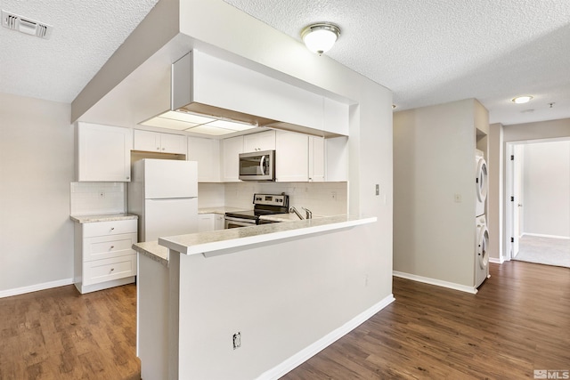 kitchen with stacked washer and dryer, appliances with stainless steel finishes, backsplash, and dark wood-type flooring