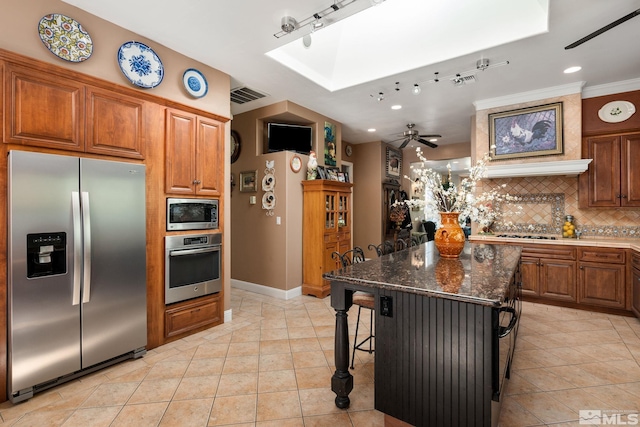 kitchen with a kitchen bar, a center island, dark stone countertops, stainless steel appliances, and backsplash