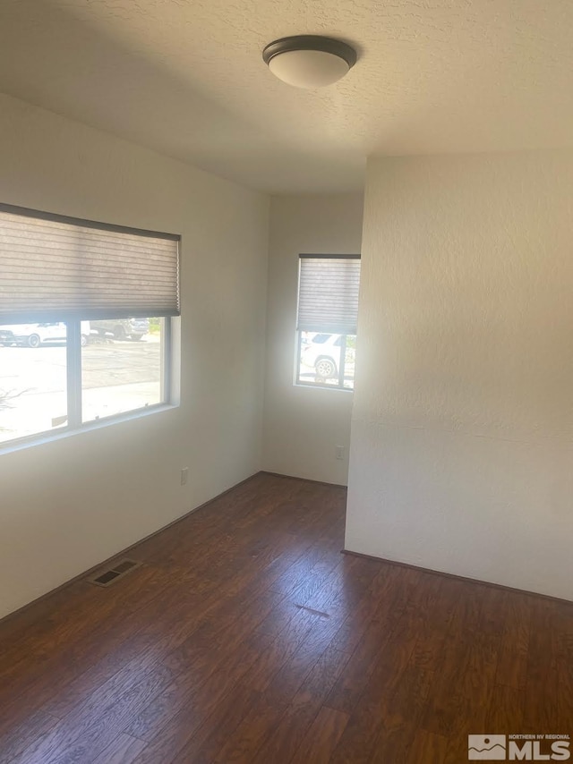 spare room with dark wood-type flooring, a wealth of natural light, visible vents, and a textured ceiling