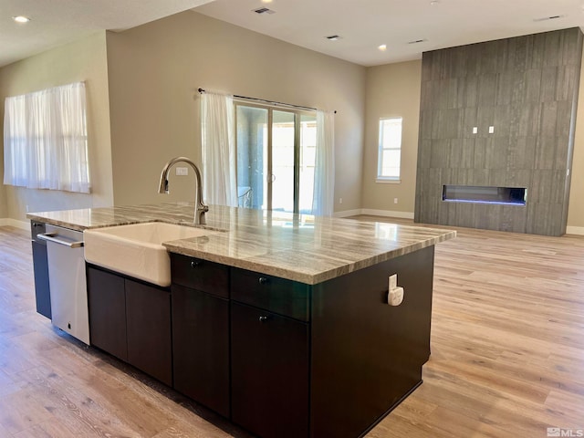 kitchen featuring light stone countertops, a fireplace, light hardwood / wood-style flooring, an island with sink, and sink