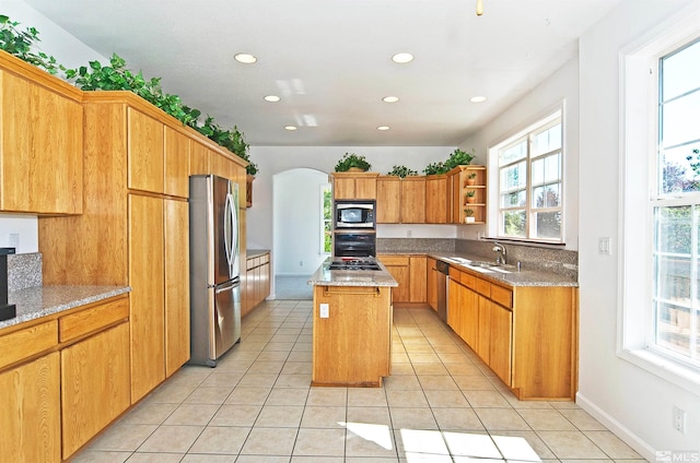 kitchen with light tile patterned flooring, stainless steel appliances, light stone counters, sink, and a kitchen island