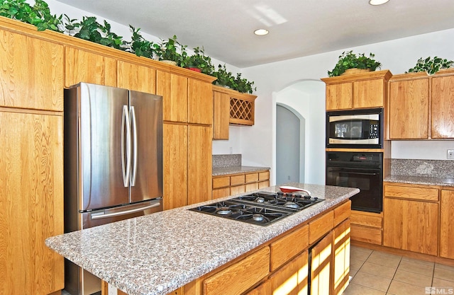 kitchen featuring black appliances, a kitchen island, light stone counters, and light tile patterned floors