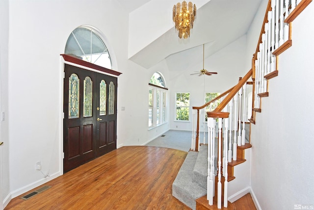 foyer with high vaulted ceiling, ceiling fan with notable chandelier, and carpet flooring