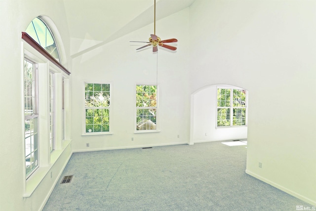 carpeted empty room with ceiling fan, high vaulted ceiling, and plenty of natural light