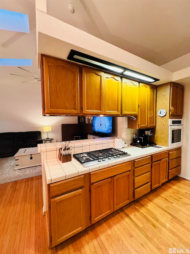 kitchen featuring light hardwood / wood-style flooring, tile counters, kitchen peninsula, and oven