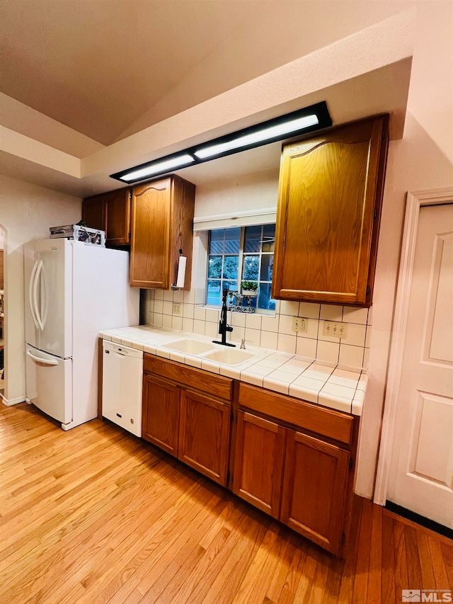 kitchen featuring tasteful backsplash, light wood-type flooring, white appliances, and sink