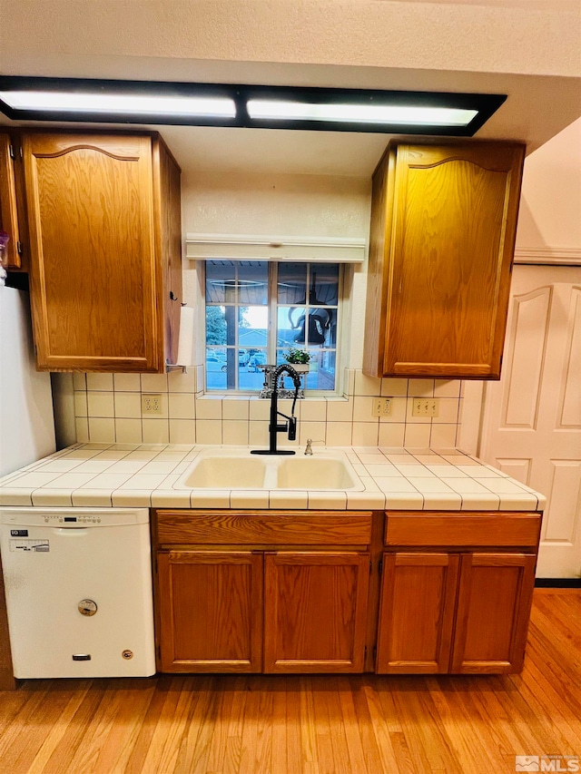 kitchen featuring light wood-type flooring, decorative backsplash, tile counters, white dishwasher, and sink