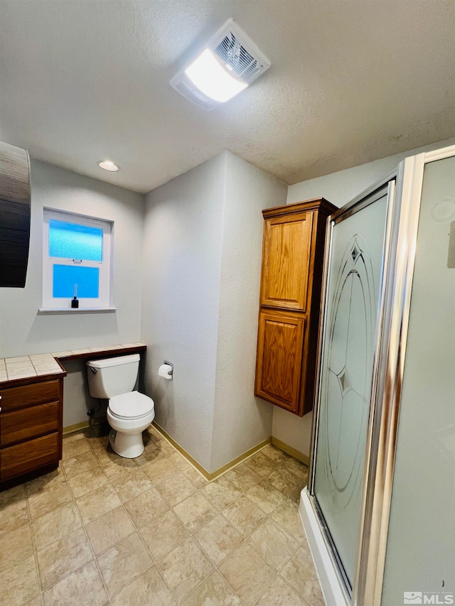 bathroom featuring a textured ceiling, toilet, tile patterned floors, and a shower with shower door