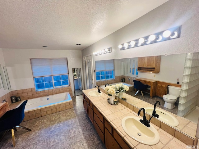 bathroom with a textured ceiling, tiled tub, toilet, and dual bowl vanity