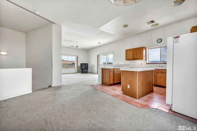 kitchen with ceiling fan, white fridge, light colored carpet, and a kitchen island