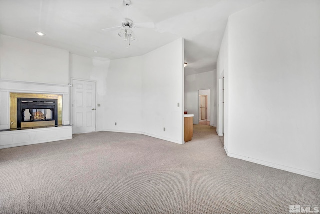 unfurnished living room featuring ceiling fan, light carpet, a multi sided fireplace, and a high ceiling