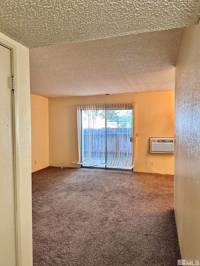 carpeted empty room featuring a wall mounted AC and a textured ceiling