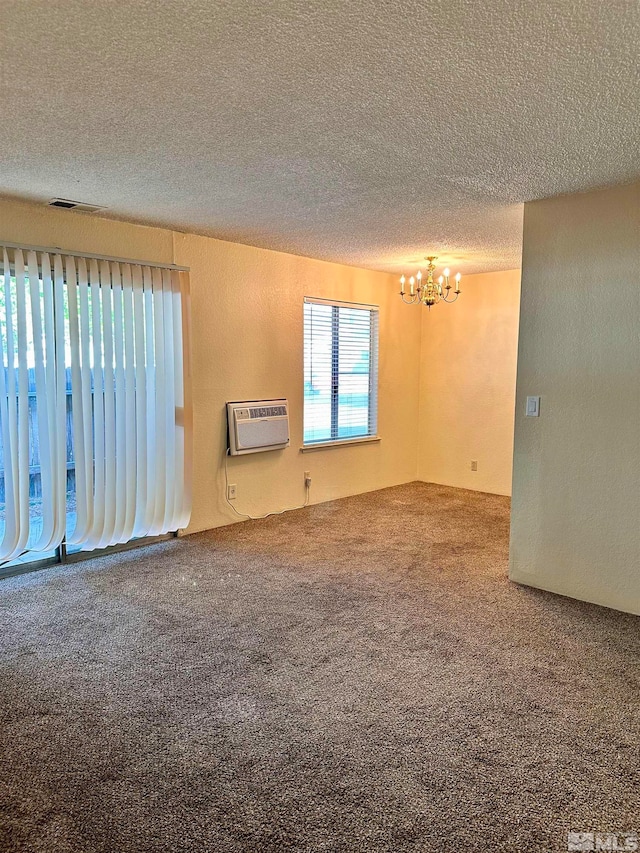 empty room with an AC wall unit, a chandelier, a textured ceiling, and carpet floors