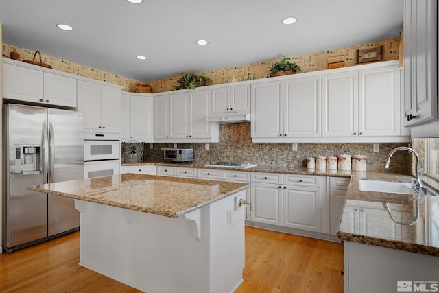 kitchen with light wood-type flooring, light stone countertops, a center island, white cabinets, and appliances with stainless steel finishes