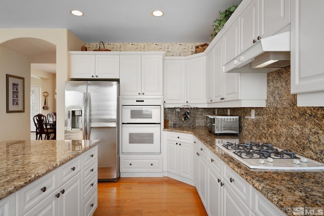 kitchen featuring white cabinets, white appliances, light hardwood / wood-style flooring, dark stone countertops, and decorative backsplash