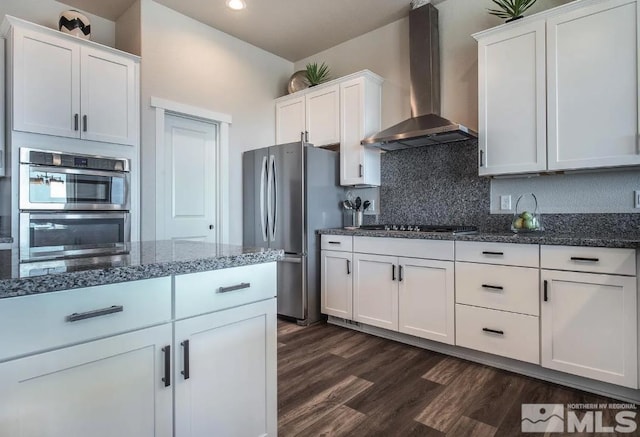 kitchen with dark wood finished floors, stainless steel appliances, wall chimney range hood, white cabinetry, and backsplash