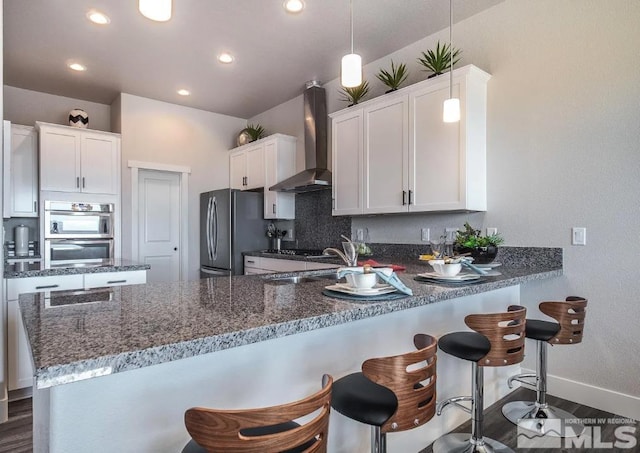 kitchen featuring stainless steel appliances, white cabinets, wall chimney range hood, and a peninsula