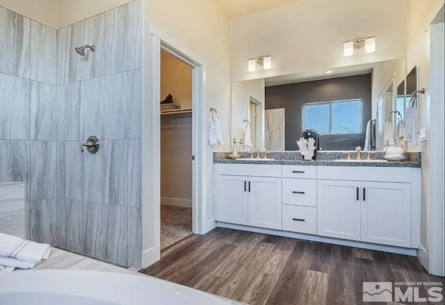 bathroom with a sink, double vanity, wood finished floors, and a tile shower