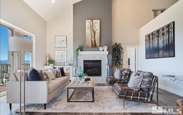 living room with high vaulted ceiling, a tile fireplace, baseboards, and wood finished floors