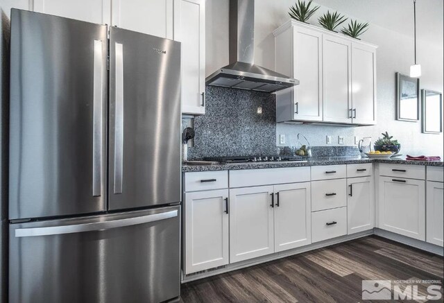 kitchen with white cabinets, dark stone countertops, stainless steel refrigerator, dark hardwood / wood-style floors, and wall chimney exhaust hood