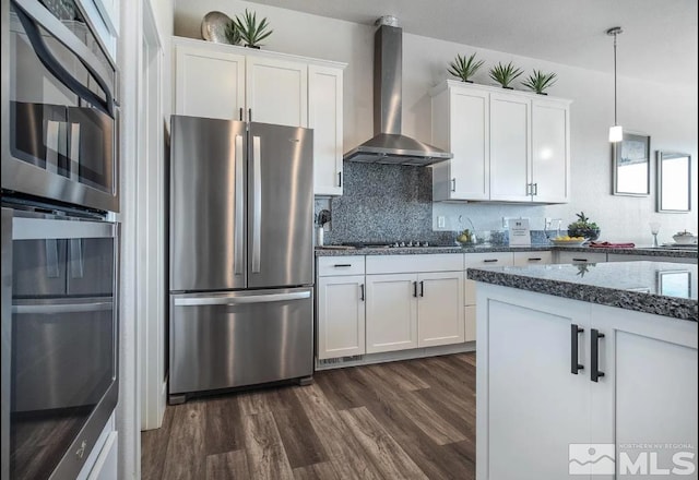 kitchen with white cabinets, freestanding refrigerator, dark stone counters, wall chimney exhaust hood, and dark wood finished floors