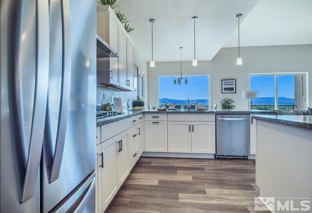 kitchen with dark hardwood / wood-style floors, wall chimney exhaust hood, appliances with stainless steel finishes, white cabinetry, and dark stone counters