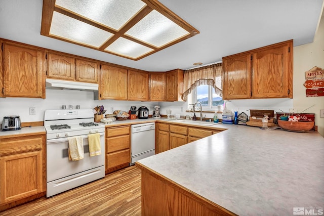 kitchen featuring white appliances, under cabinet range hood, light countertops, and brown cabinetry