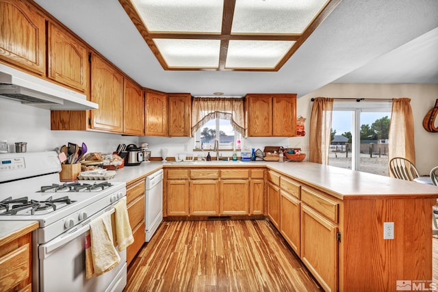 kitchen featuring under cabinet range hood, a peninsula, white appliances, light countertops, and brown cabinets