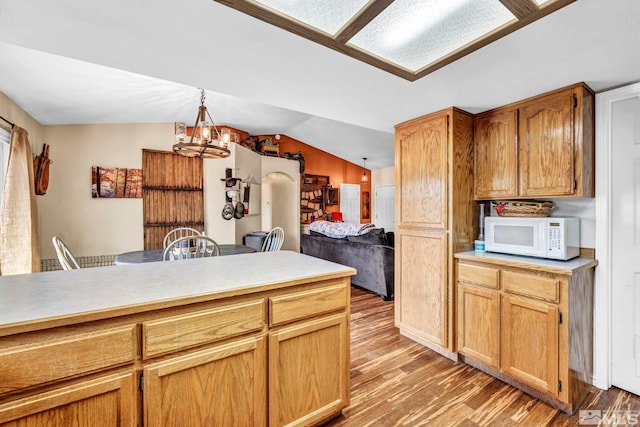 kitchen with lofted ceiling, a chandelier, white microwave, light countertops, and decorative light fixtures