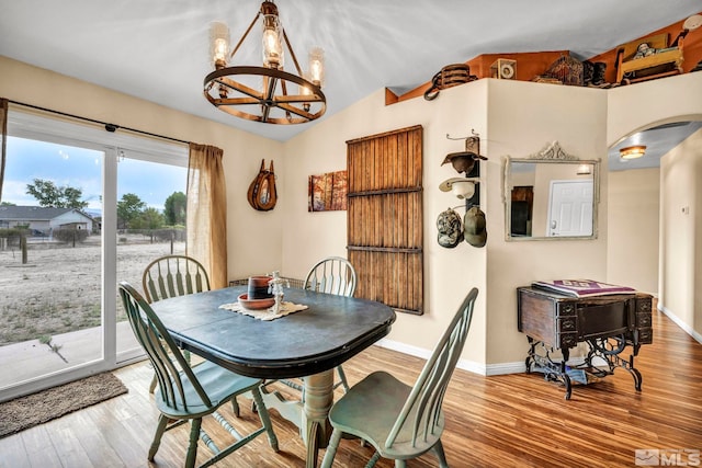 dining space with arched walkways, a chandelier, wood finished floors, baseboards, and vaulted ceiling