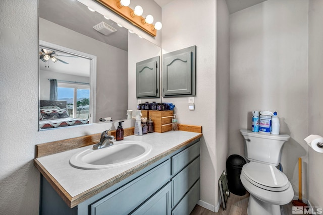 bathroom with visible vents, toilet, a ceiling fan, vanity, and baseboards