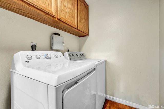 washroom featuring washing machine and dryer, cabinet space, baseboards, and wood finished floors