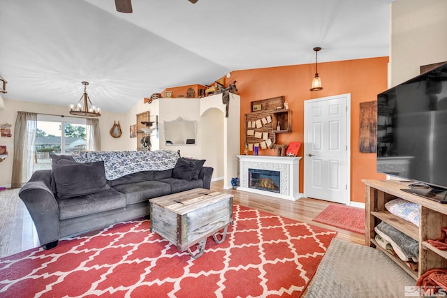 living room featuring baseboards, arched walkways, a glass covered fireplace, lofted ceiling, and wood finished floors