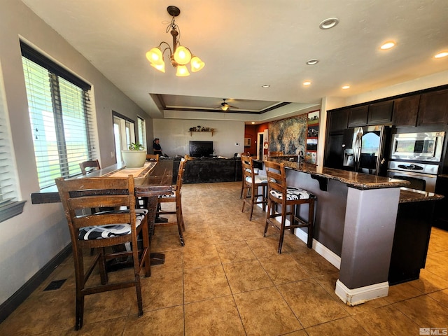 kitchen with baseboards, a raised ceiling, dark stone countertops, hanging light fixtures, and stainless steel appliances