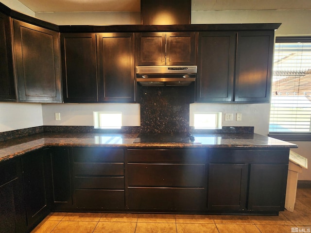 kitchen with black electric cooktop, under cabinet range hood, dark brown cabinets, decorative backsplash, and dark stone counters