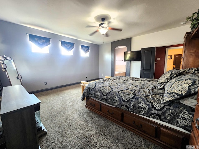 carpeted bedroom featuring arched walkways, ceiling fan, ensuite bath, and baseboards